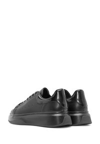 Een paar zwarte low-top leren sneaker met dikke zolen, veter sluitingen en een gladde, licht glanzende afwerking, getoond vanuit een achterhoek.