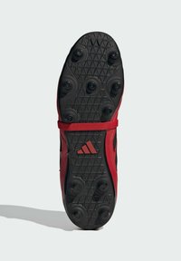 Sole di scarpa sportiva rossa con una superficie in gomma nera texturizzata, dotata di tacchetti sagomati per una migliore aderenza e una prominente cinghia centrale.