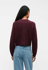 Burgundy cropped sweater made of soft, textured fabric. Features a round neckline and long sleeves, paired with light blue high-waisted jeans.