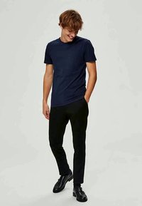 T-shirt de manga curta azul-marinho em tecido suave, combinado com calças pretas ajustadas. O modelo está de pé de forma descontraída com as mãos nos bolsos.