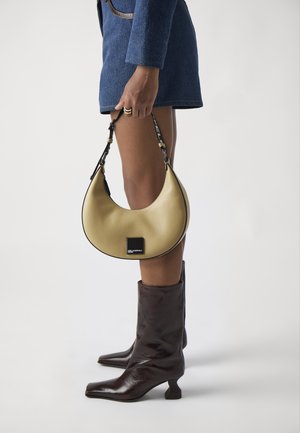 Yellow leather handbag with a crescent shape and black trim, featuring a detachable strap and a square logo patch. Brown leather knee-high boots.