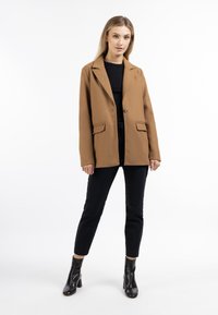 Blazer in misto lana marrone con rever a punta, chiusura con un solo bottone e due tasche anteriori, abbinato a pantaloni neri slim e stivali alla caviglia.