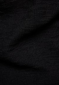 Schwarzer Textilstoff mit gerippter Struktur, der sich durch verflochtene Fäden auszeichnet, die eine subtile Tiefe und Weichheit erzeugen.