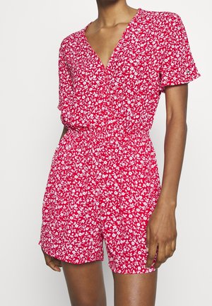 Rød kort buksedragt med blomsterprint, dyb V-hals, korte ærmer og elastisk talje. Har hvide blomsterprint over hele.