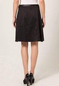 Zwarte rok met een aansluitende tailleband, plooien en een lengte tot de knie. Gemaakt van een glad materiaal, gecombineerd met zwarte hoge hakken.
