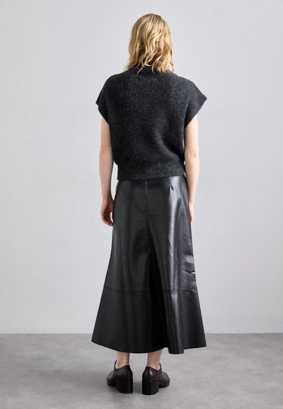 Gonna maxi nera in pelle con orlo svasato e texture liscia. Abbinata a un top di maglia scura, con maniche corte e motivo a coste.