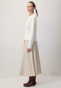 Valge kudum, millel on ümmargune kaelus, koos beeži A-line seeliku ja tume burgundia kuni põlveni ulatuvate saapastega, mis täiendavad komplekti.