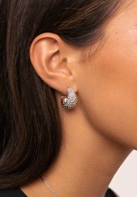 Pendientes de plata con un dise ño curvado, que presentan acentos de cristal brillante y un acabado pulido. Presentados en una oreja en vista lateral.