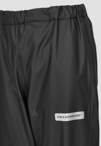 Sorte vandtætte bukser med elastisk talje og logomærke. Glat tekstur med forstærkede sømme for holdbarhed.