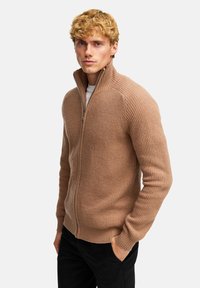 Mörk ribbad zip-up tröja med hög krage och långa ärmar. Har en figurnära design med en strukturerad tyg och subtil glans.