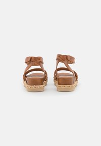 Sandali in pelle marrone con fasce incrociate, suole in stile espadrillas e tacco piatto. Presentano una fibbia regolabile alla caviglia e dettagli intrecciati.
