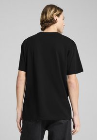 Sort kortærmet t-shirt med rund halsudskæring, vist fra ryggen. Glat stof, afslappet pasform og subtile syninger langs kanten.