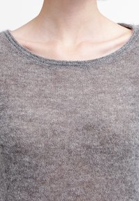 Pull en maille gris avec un col rond et une texture douce, agrémenté de coutures discrètes le long du col et du corps.