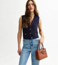 Marinblå väst med texturerat, ribbade mönster och guldfärgade knappar, tillsammans med ljusa denimjeans och en liten brun handväska.