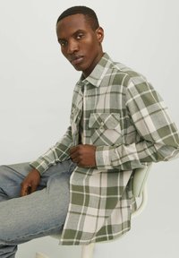 Groen-witte geblokte shirt met knoopsluiting, met een borstzak en omgeslagen mouwen, gedragen over lichtblauwe jeans.
