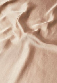 Satin fabric in a light beige color, featuring a smooth, shiny texture with soft folds and creases, showcasing its fluidity and drape.