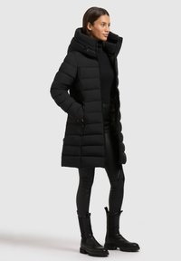 Mustast polsterdatud talvejope kõrge kraega, pikkade varrukatega ja sirge lõikega. Kanditud mustade sukkpükste ja massiivsete põlveni ulatuvate saapadega.