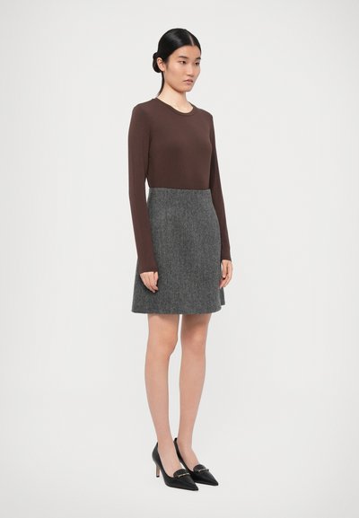 Bruine longsleeve top gecombineerd met een grijze rok met een uitlopende design. Model draagt zwarte puntige hakken met een gouden accentdetail.