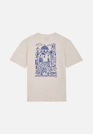 Beige T-shirt met blauwe lijntekening van mediterrane gebouwen, palmbomen, straatlantaarn en een vis vlakbij golvend water achter in het midden.