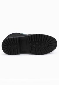 Suela de bota negra con patrón de tracción resistente, bloque rectangular en el centro y acentos azules cerca de la parte superior. Construcción de goma texturizada.