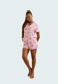 Pink pajama set featuring a short-sleeve button-up top and matching shorts, adorned with an all-over heart pattern in orange.