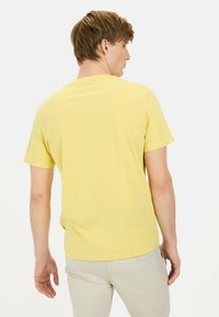 Gul kortærmet t-shirt med rund hals, lavet af bomuld, med et enkelt design og en lige kant ved livet.