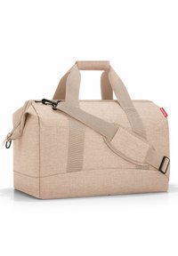 Borsa a duffel beige realizzata in tessuto testurizzato. Presenta manici doppi, una tracolla regolabile e un compartimento principale con zip. Design semplice.
