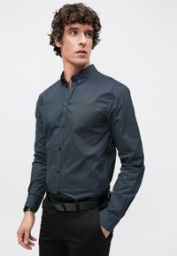 Σκούρο μπλε πουκάμισο με λευκά πουά, γιακά με αιχμηρές άκ�ρες και μακριά μανίκια. Φοριέται με μαύρο παντελόνι και μαύρη ζώνη.