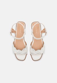 Zapatos de sandalia blancos con detalles de encaje, suela plana, diseño de punta abierta, banda en el tobillo y un forro interior marrón claro. Estilo simple y elegante.