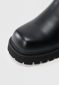 Botte en cuir noir avec un bout arrondi, une surface texturée et une semelle épaisse en caoutchouc à motif cranté pour l'adhérence.