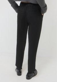 Pantaloni neri dal taglio sartoriale, con vita elastica, due tasche posteriori, texture liscia e pieghe stirate sul davanti.