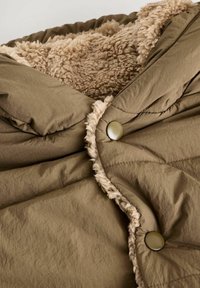 Kaki pufferjacka med en texturerad, beige fleecefoder. Har en quiltad design och runda, metallknappar på framstängningen.