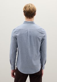 Camicia azzurro chiaro a maniche lunghe con colletto abbottonato, pince sulle spalle e bottoni sui polsini, realizzata in un tessuto strutturato.