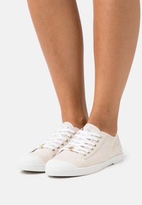 Sneakers bianchi con strisce color tan, design con lacci, suole in gomma bianche, occhielli in tonalità dorata e tessuto texturizzato. Nessun logo visibile.