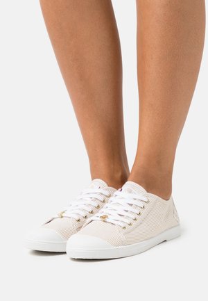 White sneakers with tan stripes, lace-up design, white rubber soles, gold-tone eyelets, and textured fabric. No visible logo.