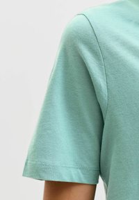 Lichtgroen katoenen T-shirt met een ronde hals en korte mouwen. Zachte textuur met een nette zoom en een ingetogen ontwerp.