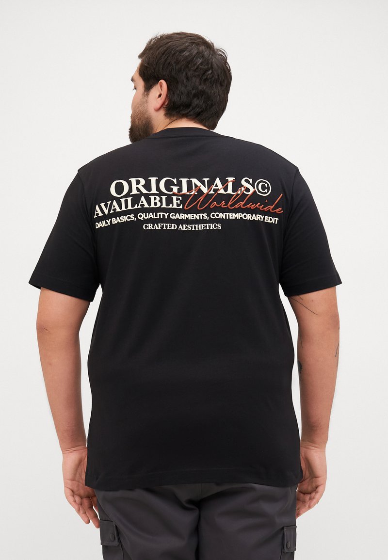 Tricou scurt cu mânecă neagră, având text alb și roșu pe spate. Textul spune „ORIGINALS AVAILABLE Worldwide”, împreună cu detalii suplimentare de brand.