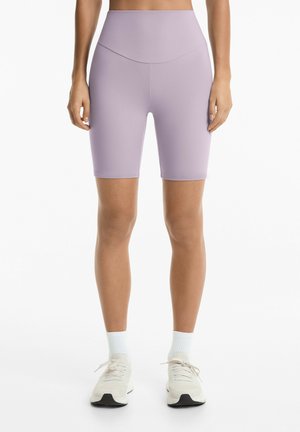Lila fietsbroek met hoge taille, gladde textuur, knielange pasvorm, gecombineerd met beige sneakers en witte crew-sokken.