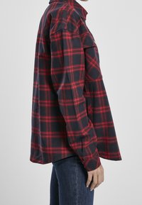 Röd och marinblå rutigt flanellskjorta med knäppdesign, två bröstfickor och långa ärmar. Lång mjuk textur och avslappnad passform.