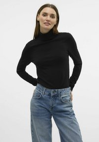 Črn pulover z visokim ovratnikom, izdelan iz mehkega blaga, v kombinaciji z svetlo modrimi kavbojkami z visokim pasom. Kavbojke imajo ohlapen kroj in zasnovo z petimi žepi.