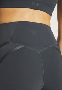 Wysokie, ciemnoszare legginsy sportowe o gładkiej fakturze, z akcentami logo i usztywnioną talią.