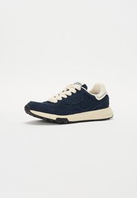 Adidași din suede bleumarin cu sireturi și accente crem, cu un finisaj texturat și talpă din cauciuc. Brandingul cunoscut este vizibil pe lateral și pe limbă.