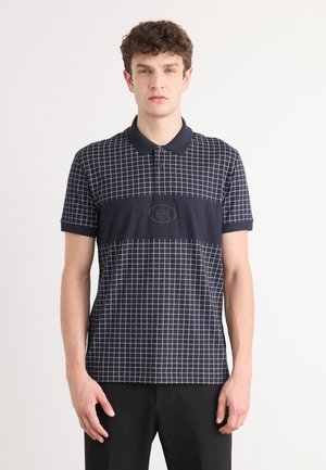 Polo bleu marine avec un motif à carreaux blancs, à manches courtes et col. Présente un écusson logo sur la poitrine, fabriqué à partir d'un mélange de tissus lisses.