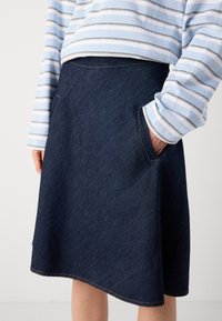 Mørkeblå denimskjørt med A-linjeform, som har sidelommer og kontrastsøm langs kanten.