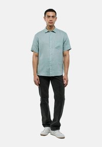 Chemise à manches courtes, vert menthe clair avec un devant à boutons et une poche poitrine, associée à un jean sombre et des baskets blanches. Texture de tissu lisse.