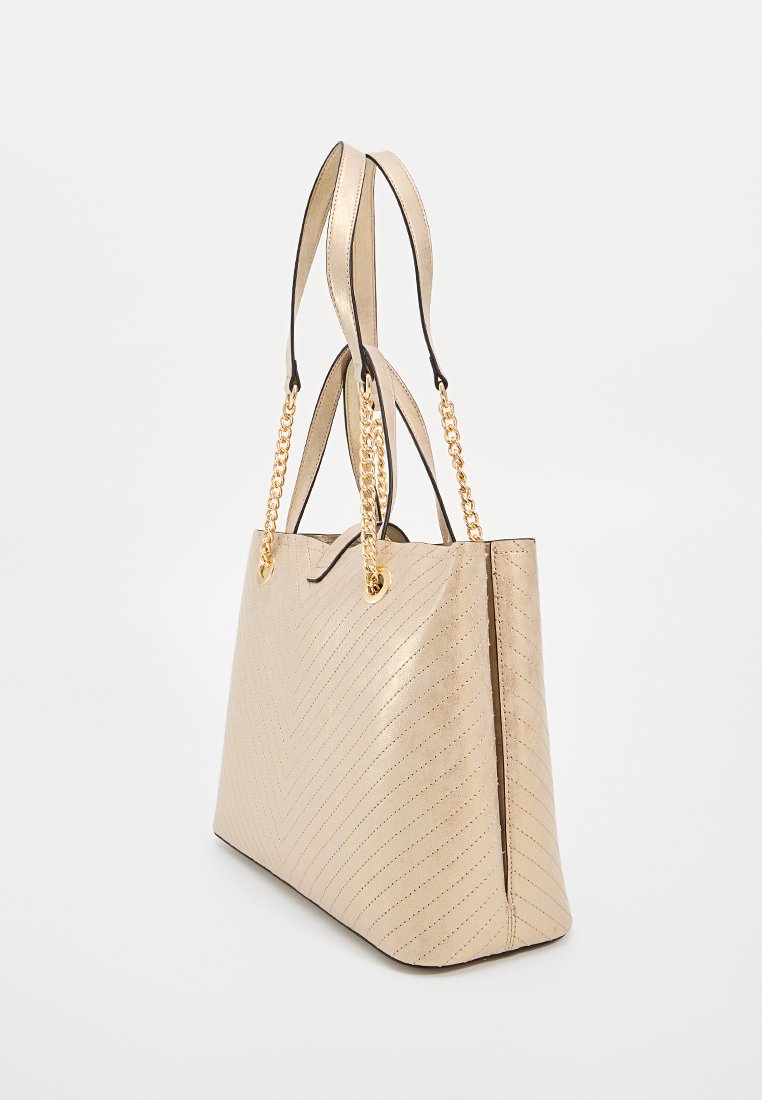 Bolso tote beige con un patrón de chevron, hecho de material texturizado. Cuenta con dos asas y acentos de cadena dorada. Forma rectangular.