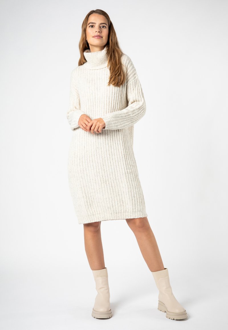 Cremfarbendes, geripptes Rollkragenkleid mit langen Ärmeln, knielanger Schnitt, kombiniert mit beigefarbenen Ankle-Boots mit dicker Sohle.