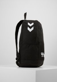 Zaino nero realizzato in tessuto resistente, con motivi a zigzag bianchi, una tasca laterale con zip e spallacci regolabili. Design semplice e funzionale.