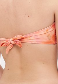 Pink tie-dye bikini top with a knotted back detail and small logo on the side, made of smooth, stretchy fabric.