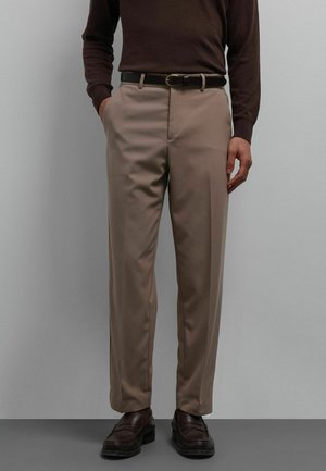 Beige broek met rechte snit, gladde textuur, voorzakken en een zwarte riem. Gecombineerd met een bruine top met lange mouwen en donkere schoenen.